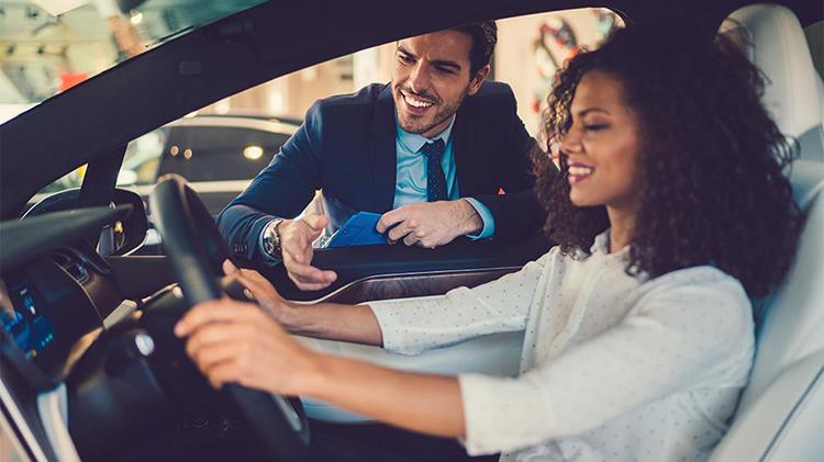 Woman considering buying a car while salesman leans in the window.